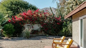 A patio with two yellow cushioned chairs, a gravel ground, and a wall covered with red flowers and cacti. - The Yorba Oasis w/Pool (Palm Springs)