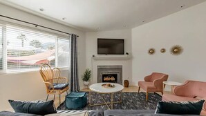 A modern living room with a fireplace, a TV mounted above it, and a seating area with a sofa and chairs. - The Yorba Oasis w/Pool (Palm Springs)
