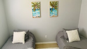 A bedroom with two beds, each with a gray blanket and a white pillow. There are two framed paintings of palm trees on the wall. - Cush Jax Baymeadows Ranch, Close to Everything! (Jacksonville)