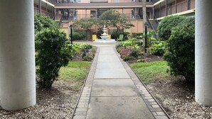 A courtyard with a central pathway, surrounded by greenery and a water feature. - Oceanfront condo with beach view – 2 pools (Galveston)