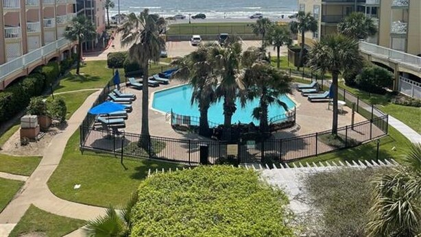 A resort with a central pool surrounded by palm trees, a beach view, and multiple buildings. - Oceanfront condo with beach view – 2 pools (Galveston)