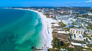 Vista aérea de una zona turística costera con propiedades frente a la playa, una playa de arena y un océano azul claro.