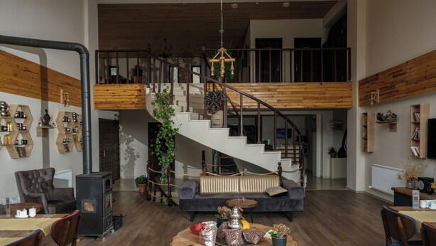 A spacious living area with a high ceiling, a staircase leading to an upper level, and a dining area with a round table and chairs. - Savsat Kosk Otel (Savsat)