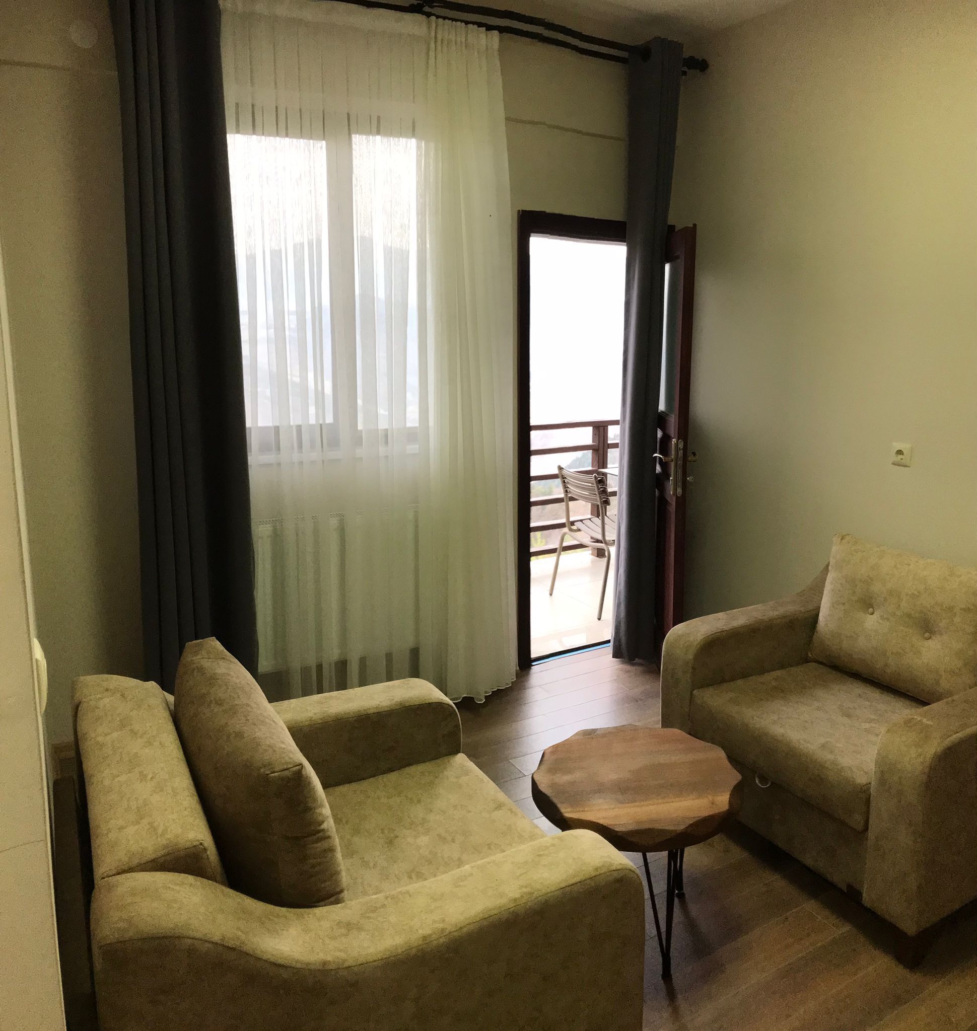 Uma sala de estar com dois sofás, uma mesa de madeira pequena e vista para uma varanda com uma cadeira.