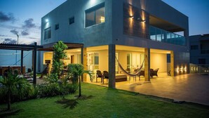 Une maison moderne à deux étages dotée d’un vaste patio, d’un espace salon extérieur et d’un hamac.