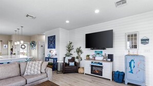 A living room with a sofa, a coffee table, a fireplace, a television, and a decorative cabinet. - Great Location, Fenced Yard, Pet Friendly! Low Rate! (Surfside)