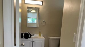 A bathroom with a white vanity, a toilet, a mirror, and a light fixture above the mirror.