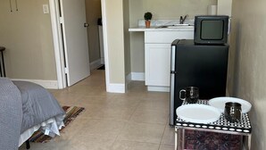 A compact room with a bed, a small table with dishes, a television, and a kitchenette.