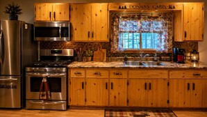 A kitchen with wooden cabinets, stainless steel appliances, a window with a patterned curtain, and a welcome sign. - NEW!! Clean, Comfortable & Spacious Northwoods Cabin. (Florence)