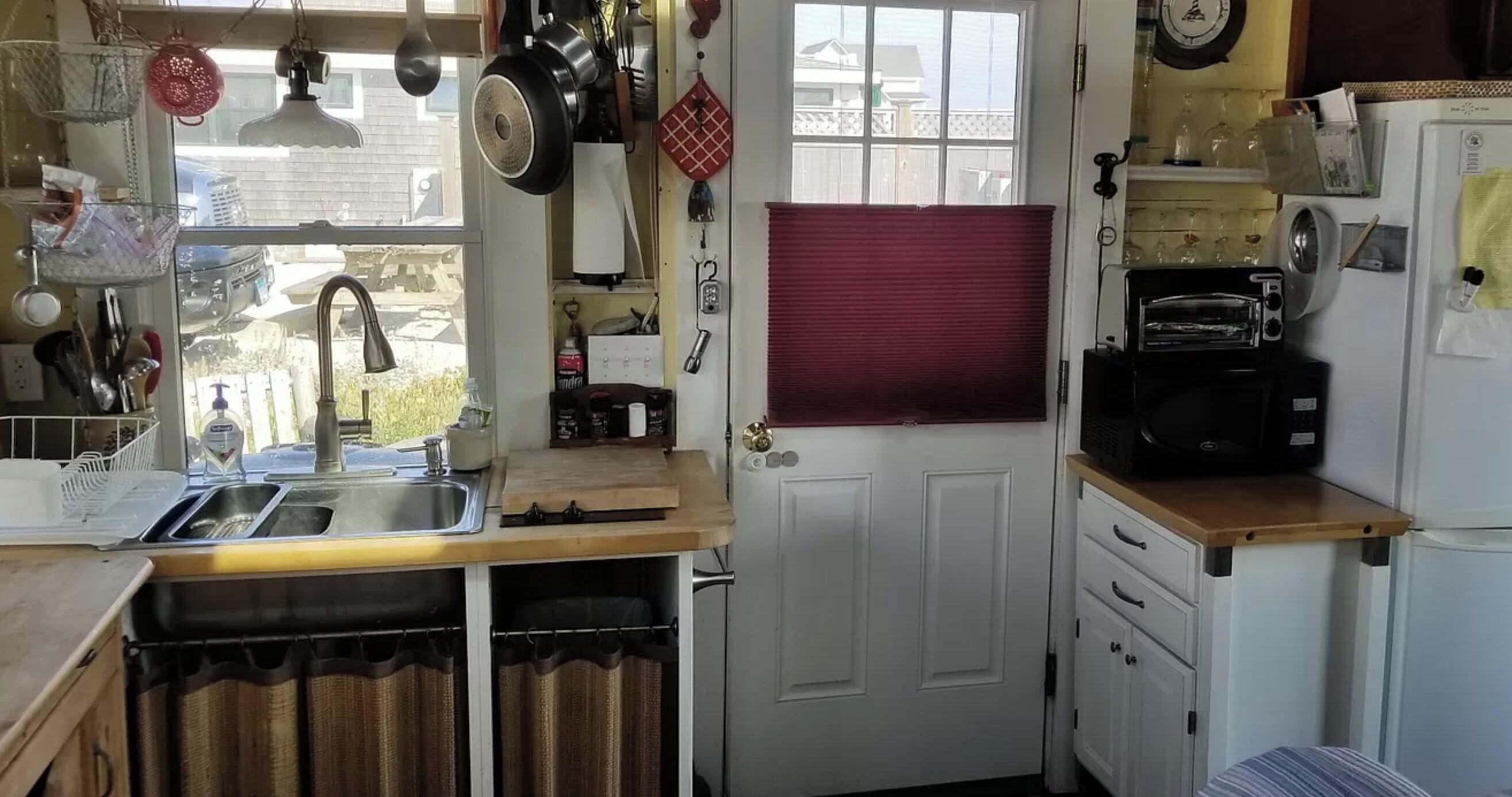 Een kleine keuken met een spoelbak, fornuis en een raam met zonwering.