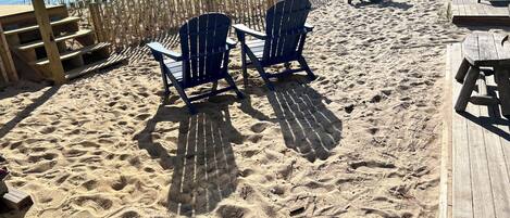 A beachside area with wooden deck seating and chairs, a wooden fence, and a view of the sea.