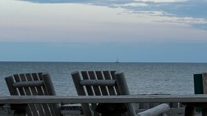 A wooden deck with two chairs facing a calm sea and a sailboat in the distance.