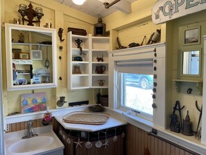 A rustic bathroom with a sink, mirror, and shelves with various items.