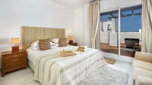 Een slaapkamer met een groot bed, twee nachtkastjes, een raam met gordijnen en uitzicht op een terras met tuinmeubilair.