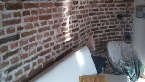 Ein Zimmer mit einer weißen Couch, einem gelben Kissen, einer Ziegelwand und einer Holzbalkendecke.