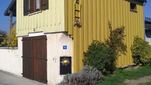 Ein gelbes Gebäude mit brauner Tür und Fensterläden, einem kleinen Fenster und einer Leiter an der Seite.