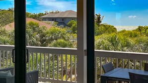 A balcony with a view of a house, lush greenery, and a clear sky. - Spectacular beach front views with a short walk to members only beach (Upper Captiva)