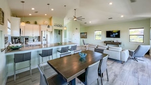 A modern kitchen with a central island, dining area with chairs, a sofa, and a TV in the living room. - Spectacular beach front views with a short walk to members only beach (Upper Captiva)