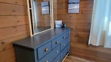 A wooden-paneled room with a dark blue dresser, a mirror, and a small table with bottles.