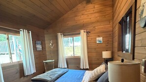 Et soveværelse i en træhytte med en seng, et natbord, en lampe og en loftsvifte.