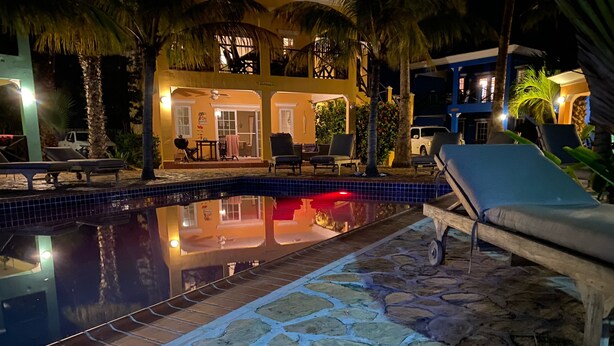 A nighttime pool area with lounge chairs, a stone pathway, and a building with a balcony. - Casa Makoshi An oasis of tranquility in Divers Paradise (Hato)