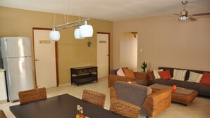 A modern living room with a dining area, featuring wicker furniture, a sofa set, and a ceiling fan. - Casa Makoshi An oasis of tranquility in Divers Paradise (Hato)