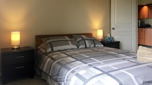 Un dormitorio con una cama, dos mesitas de noche, una pequeña cocina y una puerta.