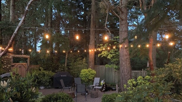 Un espacio de patio al aire libre con luces colgantes, una parrilla y asientos.