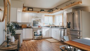 A modern kitchen with white cabinets, stainless steel appliances, wooden accents, and a central island. - Big Sky Escape: Spacious Home on Working Ranch (Reed Point)