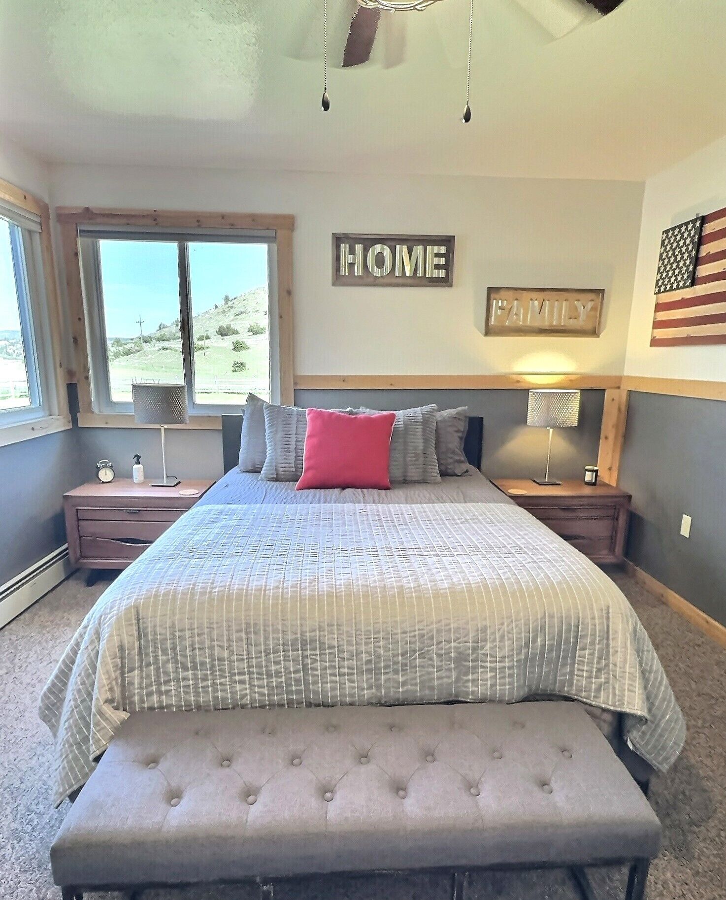A bedroom with a bed, a bench, a nightstand, a lamp, and a window with a view of a landscape.