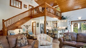 A spacious living area with a wooden staircase, leather sofas, a patterned armchair, and a kitchen in the background.