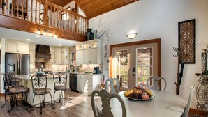 A spacious kitchen with high ceilings, a dining area with a round table, and a view through a large window.