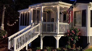 A white house with a covered porch, a staircase leading to the porch, and a small garden with pink flowers.