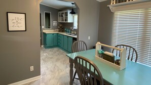 A dining area with teal cabinets, a table, and chairs. There is a sign on the wall and a window with blinds.