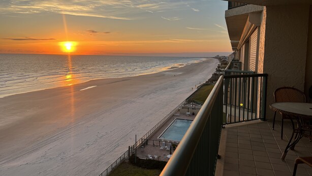 Ein Balkon mit Blick auf Strand und Meer bei Sonnenuntergang.