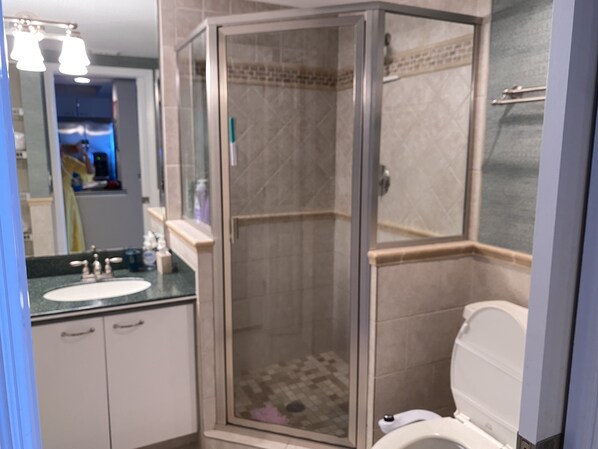 A modern bathroom with a glass-enclosed shower, a sink with a marble countertop, and a toilet.