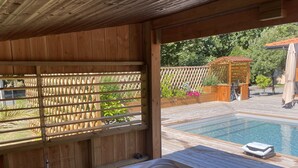A hot tub with a wooden deck, a pool, and a wooden pergola with plants.