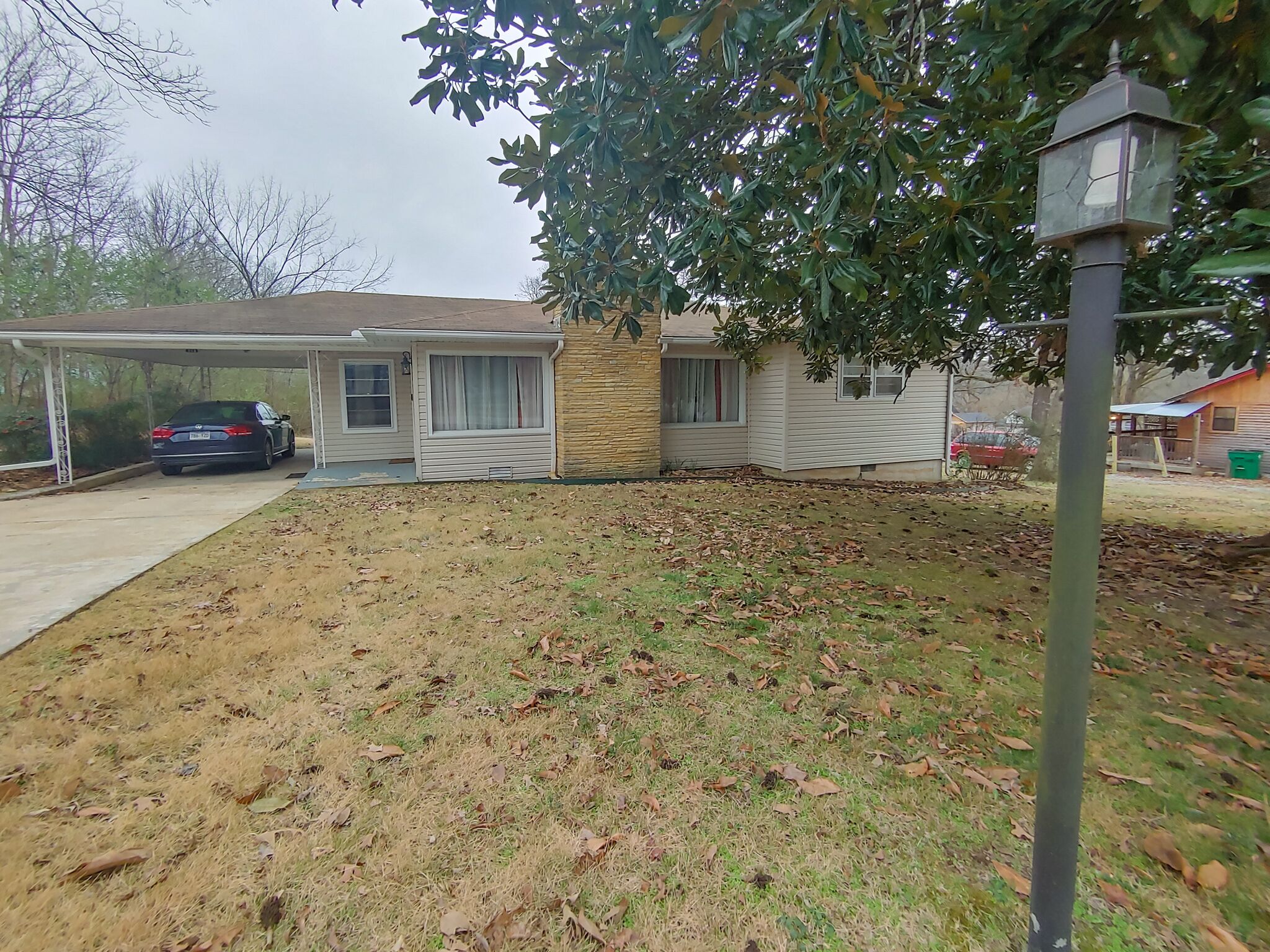 Une maison à deux étages avec un garage fermé et une cour avant où l’herbe est sèche et où jonchent des feuilles mortes.