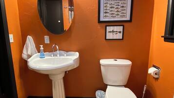 Un baño con lavamanos pedestal, inodoro e ilustración enmarcada de un pez en la pared.