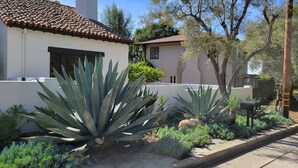 Ein Haus mit Ziegeldach, weißer Fassade und Garten mit Agavenpflanzen und Sträuchern.
