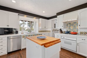 A modern kitchen with white cabinets, a wooden island, and a tiled backsplash.