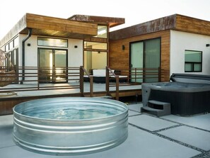 Un espace piscine extérieur moderne, doté d’un jacuzzi, d’une terrasse en bois et d’un bâtiment aux grandes fenêtres.