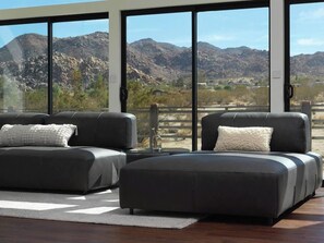 A modern living room with two sofas and a coffee table, large windows with a mountain view, and a wooden floor. - Panoramic Heaven - Luxury Property Pool & Spa (Joshua Tree)