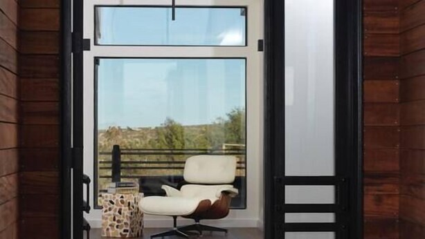 A modern entrance with a glass door, a wooden deck, and a white chair outside. - Panoramic Heaven - Luxury Property Pool & Spa (Joshua Tree)