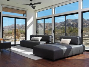 A modern living room with a large window, a ceiling fan, and a view of a mountainous landscape. - Panoramic Heaven - Luxury Property Pool & Spa (Joshua Tree)
