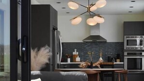 A modern living room with a black sofa, a glass coffee table, and a dining area with a wooden table and chairs. - Panoramic Heaven - Luxury Property Pool & Spa (Joshua Tree)