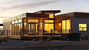 A modern building with large windows, a covered outdoor seating area, and a staircase leading to the entrance. - Panoramic Heaven - Luxury Property Pool & Spa (Joshua Tree)