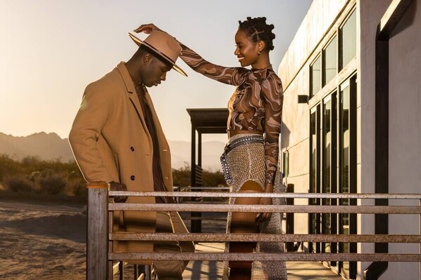 A man and a woman standing by a metal fence in front of a building with large windows. - Panoramic Heaven - Luxury Property Pool & Spa (Joshua Tree)