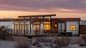 A modern house with large windows and a flat roof, surrounded by desert vegetation. - Panoramic Heaven - Luxury Property Pool & Spa (Joshua Tree)