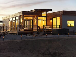 A modern building with large windows, a covered outdoor seating area, and a staircase leading to the entrance. - Panoramic Heaven - Luxury Property Pool & Spa (Joshua Tree)